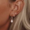 Woman showcases the Bronte Earrings which showcase a pearl drop charm